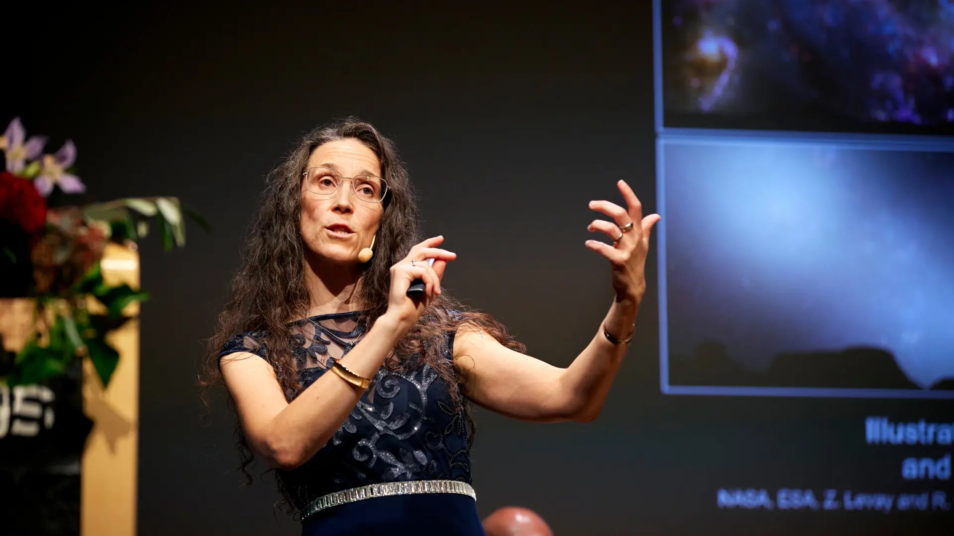 A woman speaks on stage, using her arms and hands to emphasise what she is saying.