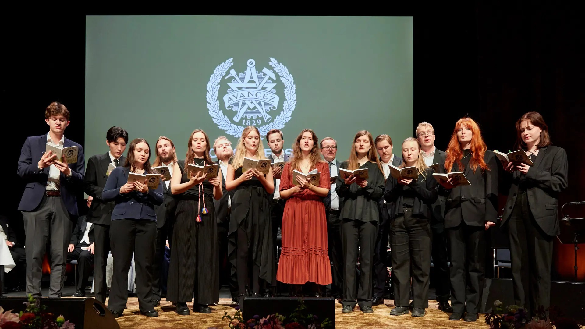 A large number of people are standing together and singing. In their hands they hold small songbooks.