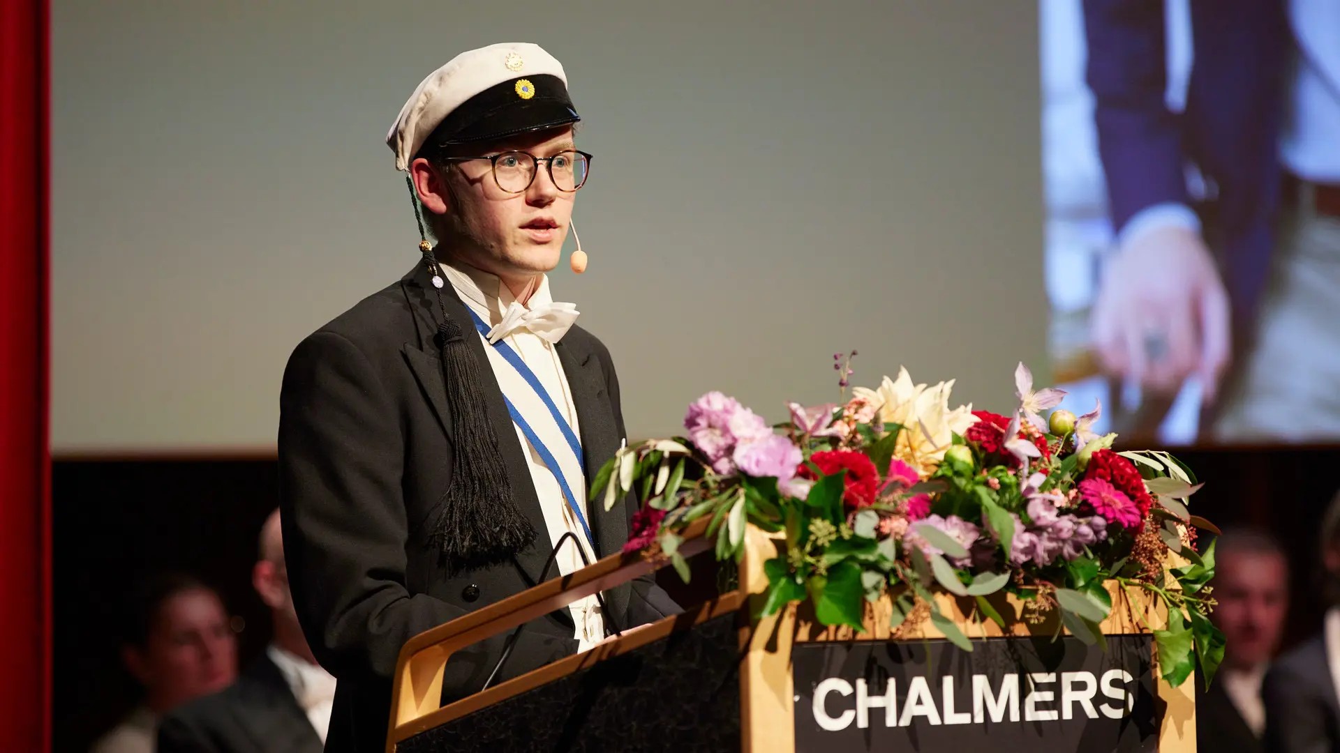 A man in a Chalmers student cap stands behind a podium.